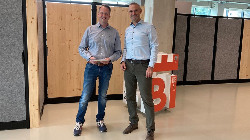 Einkäufer Tobias Jansen und LIST Bau Bielefeld Geschäftsführer René Konrad stehen im Büro in Bielefeld. René gratuliert Tobias zum Jubiläum bei LIST.